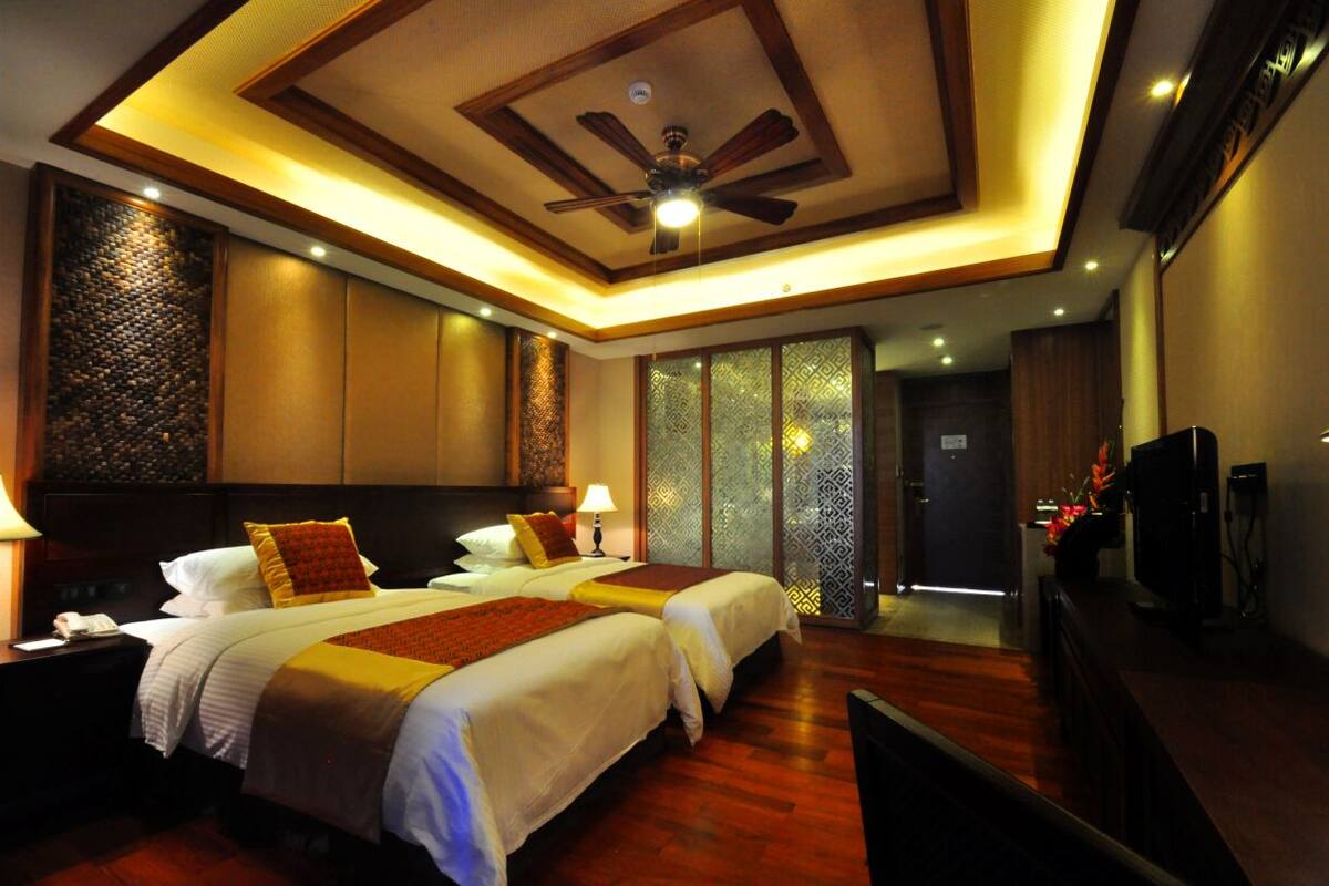 Habitación de hotel con dos camas, ventilador de techo, televisión y piso de madera.