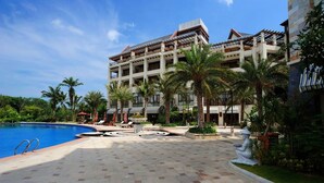 Un resort con piscina, palmeras y un edificio con varios balcones.