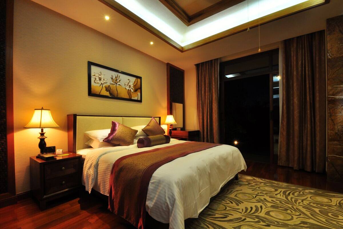 Habitación de hotel con una cama grande, dos mesitas de noche con lámparas, un cabecero, un cuadro en la pared y una alfombra estampada.