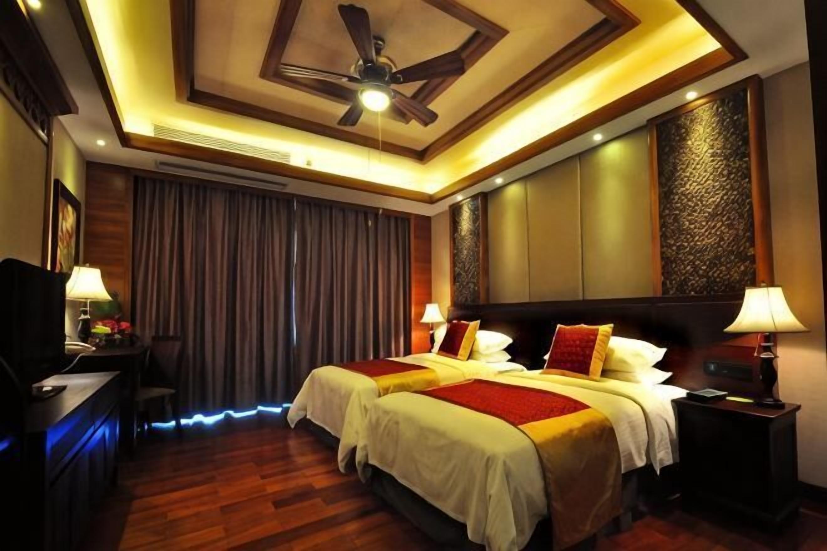 A hotel room with two beds, a ceiling fan, a desk with a lamp, and a TV.