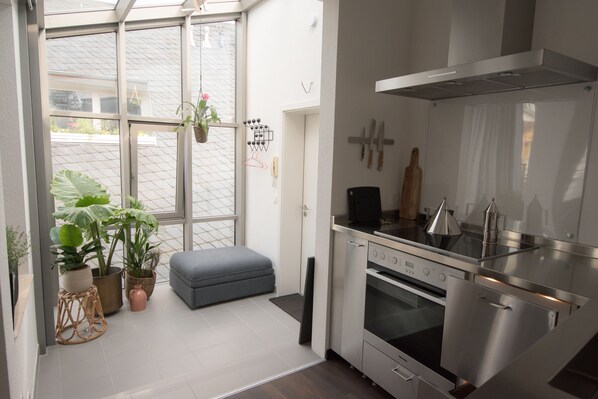 A modern kitchen with a built-in oven, a stainless steel range hood, and a large window with potted plants. - Weimar Central Artist Loft (Weimar)