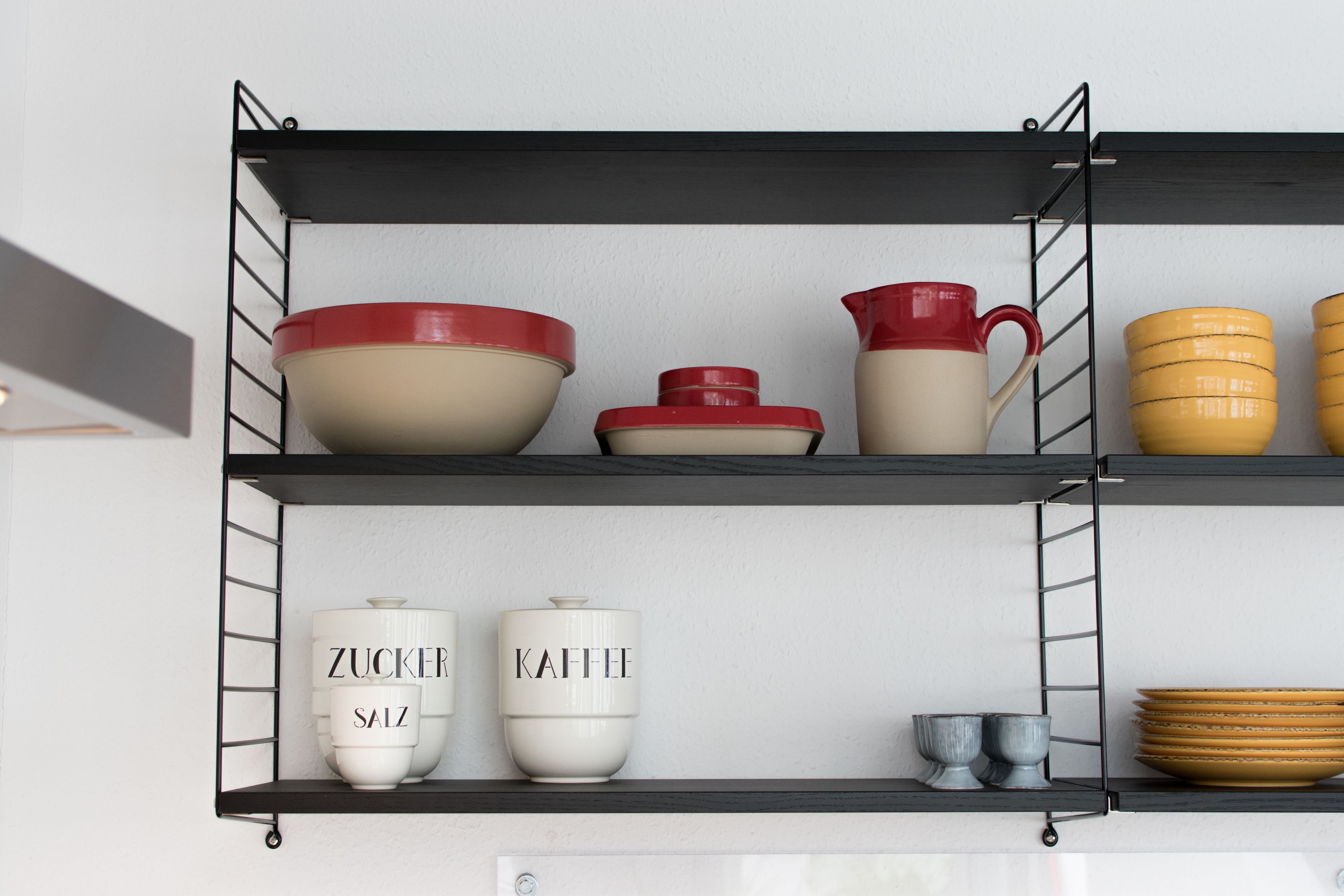 A kitchen shelf with various kitchenware items including bowls, a pitcher, and containers.