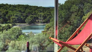 A terrace with a bottle of wine and glasses on a round table, overlooking a lake and forested hills.