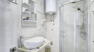 A modern bathroom with a large white sink, a glass-enclosed shower, and a white toilet.