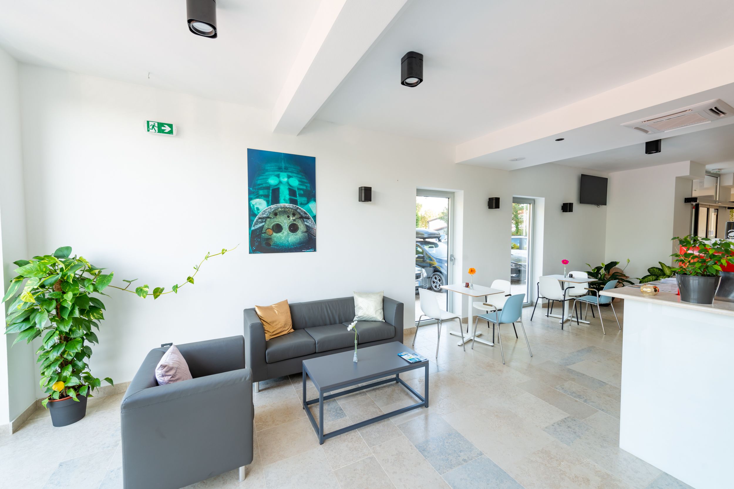A modern hotel lobby with a grey sofa, a coffee table, and a dining area with white chairs and a table.