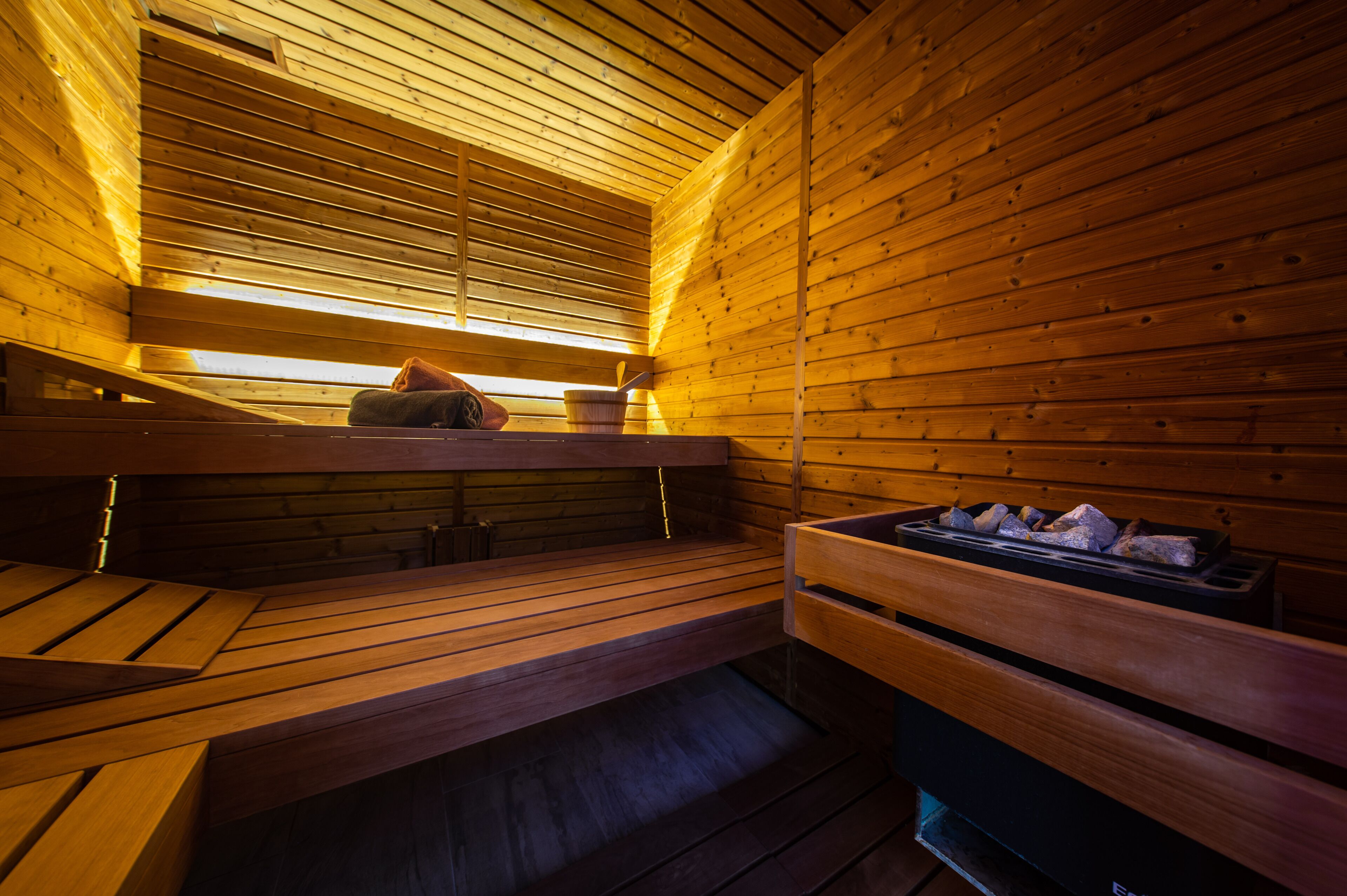 A wooden sauna with benches and a bench with a tray of stones.