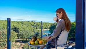 A woman sitting on a balcony with a table of fruit and a cup, overlooking a scenic landscape.
