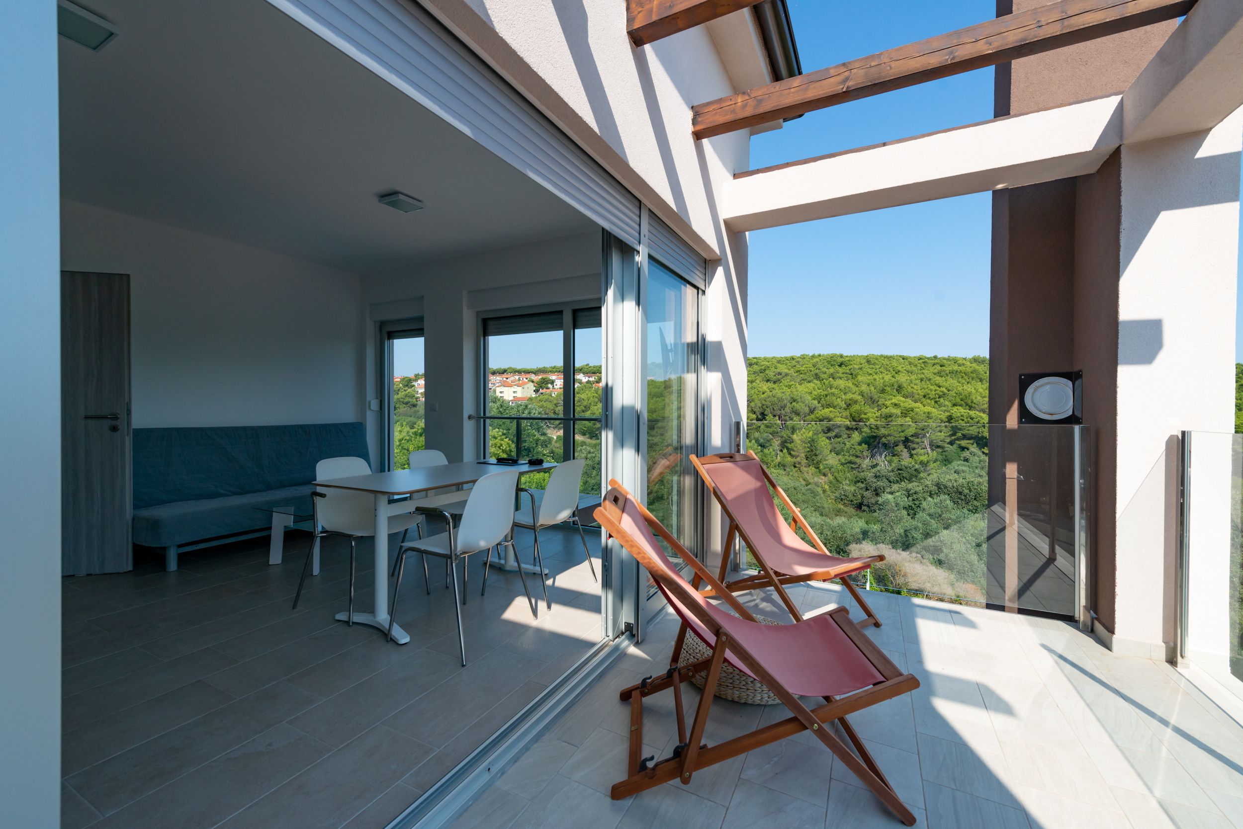 Een modern interieur met een eethoek, een bank en een balkon met uitzicht op groen.