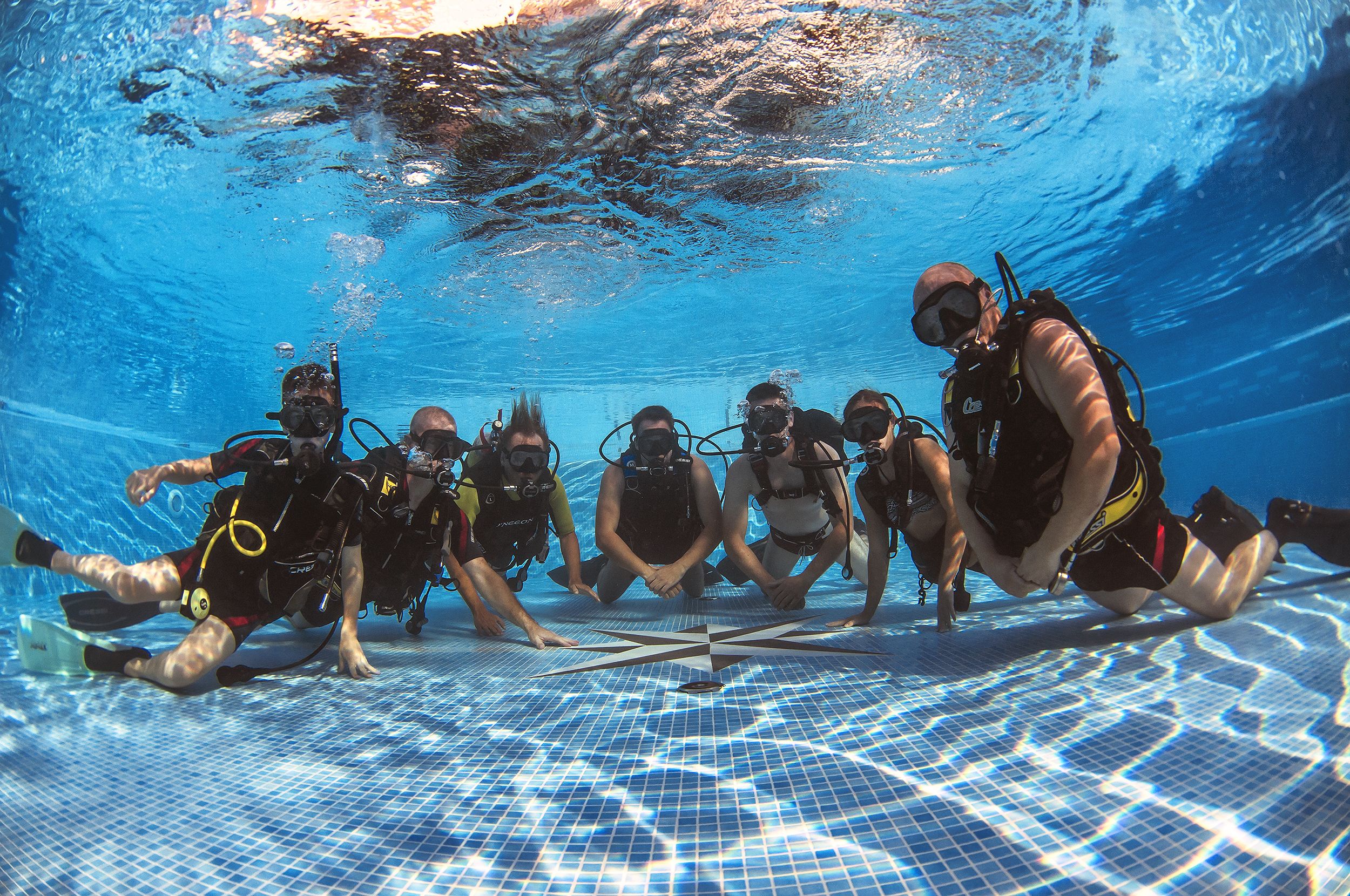 Un grupo de buzos bajo el agua en una piscina con suelo de baldosas.