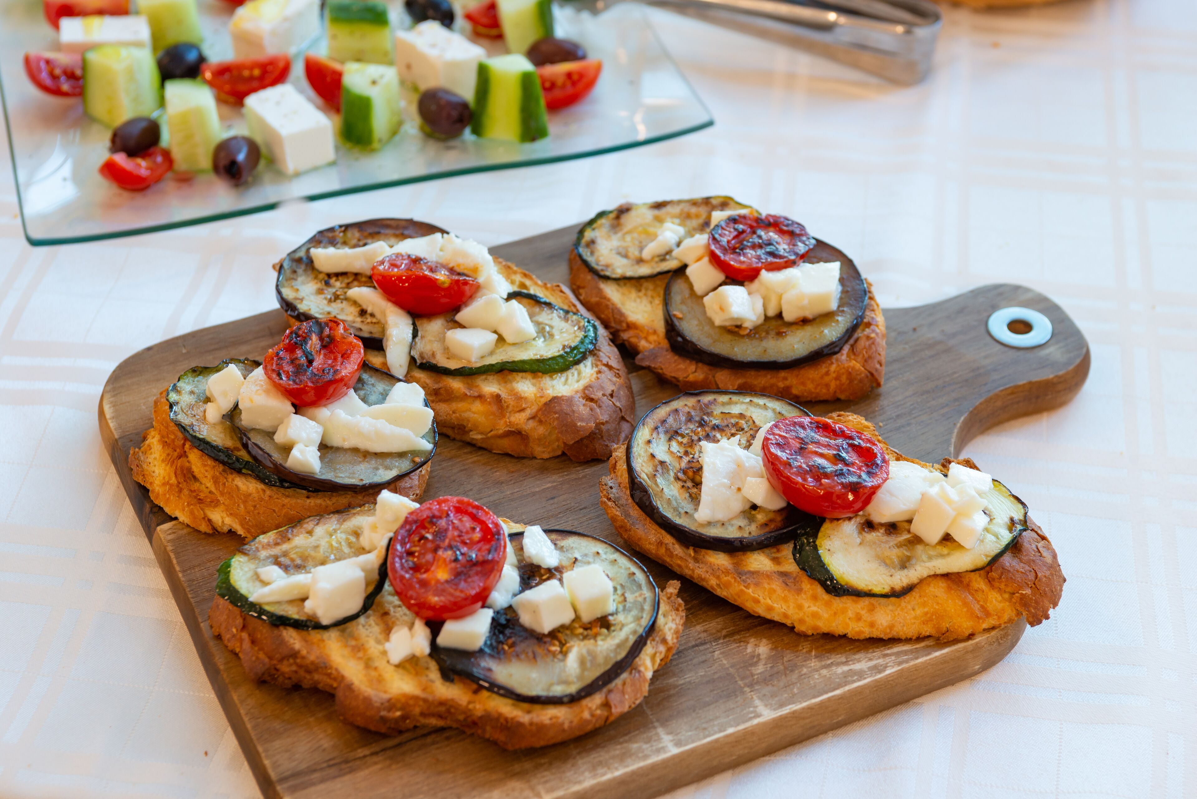 Una tabla de madera con tostadas cubiertas de verduras a la parrilla.