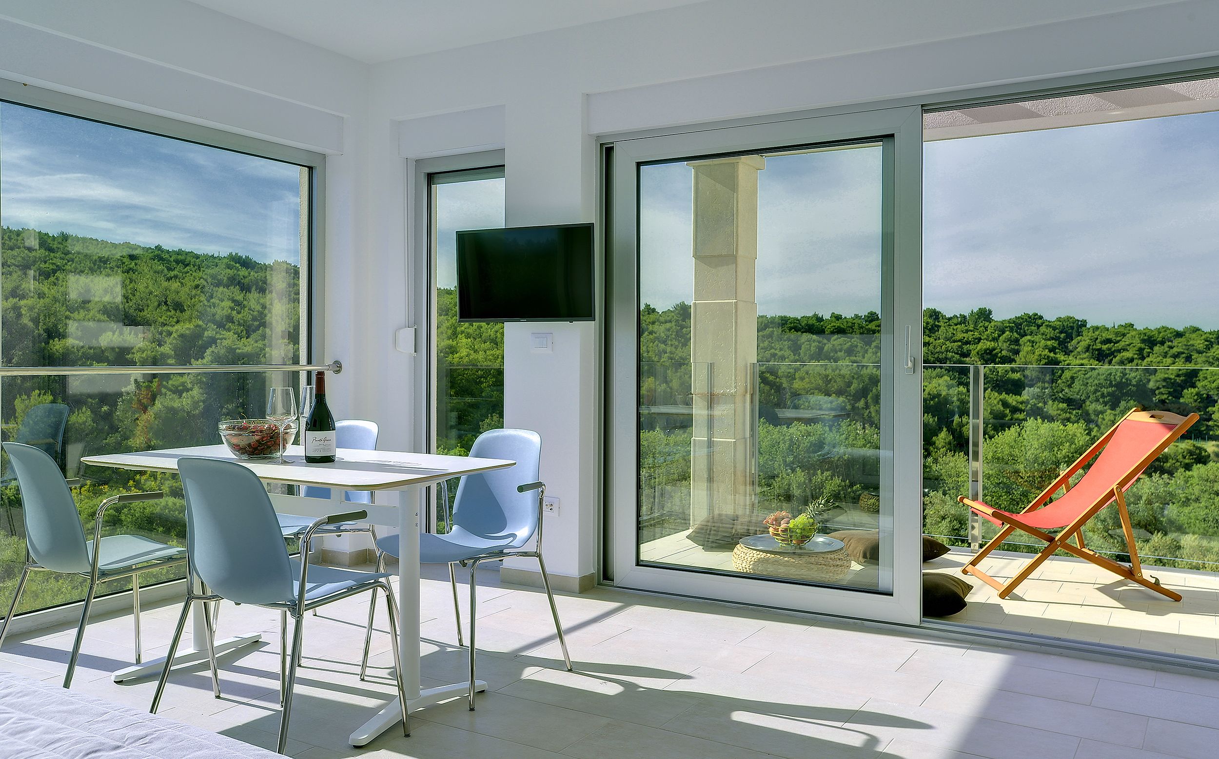 A balcony with a table, chairs, a bottle of wine, and a TV.