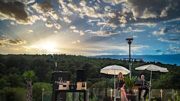 Un escenario con instrumentos musicales y altavoces, con un paisaje montañoso y un cuerpo de agua como fondo.