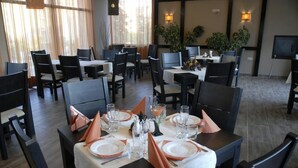 Un restaurante con varias mesas dispuestas para comer, con manteles blancos, servilletas anaranjadas y copas de vidrio transparentes.
