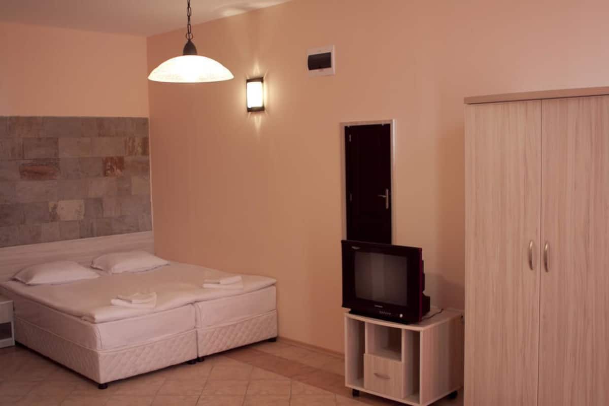 A bedroom with a bed, a television on a stand, a wardrobe, and a wall-mounted light fixture.