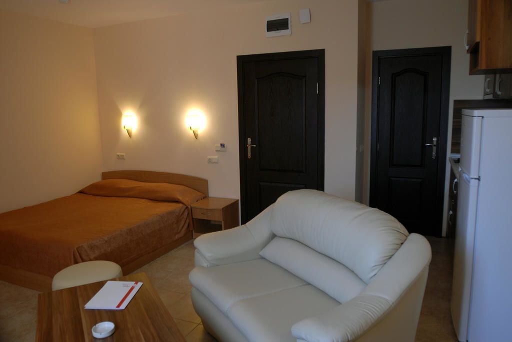 A hotel room with a bed, a sofa, a small table with a book, and a refrigerator.