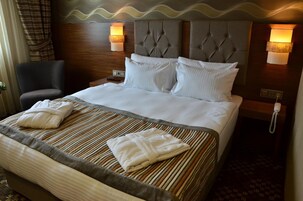 Una habitación de hotel con una cama grande, dos lámparas de noche, una silla y un teléfono.