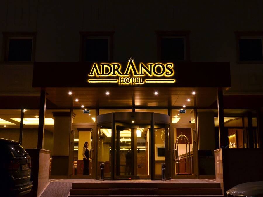 L’entrée de l’hôtel ADRANOS, avec une porte tournante et un panneau indiquant « SORTIE ».