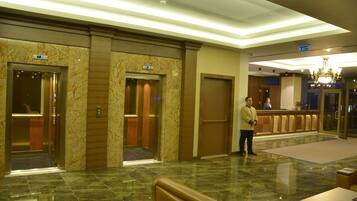 A lobby with marble flooring, elevators, a reception desk, and a chandelier.