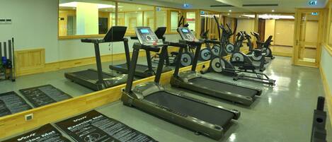 Un gimnasio con cintas de correr, colchonetas de ejercicio y un espejo grande.