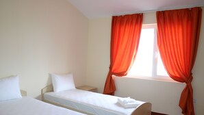 A room with two single beds, a window with orange curtains, and a small bedside table. - Prestige City Apart Hotel (Sunny Beach)