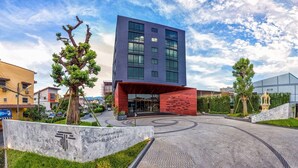 Ein moderner Hotelzugang mit einer auffälligen Glasfassade, rotem Backstein und einer begrünten Auffahrt.