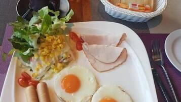 A breakfast plate with eggs, ham, sausages, corn, salad, and toast.