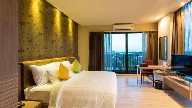 A hotel room with a large bed, a desk, a TV, and a balcony with a city view. - Ton Aoi Grand Hotel (Hat Yai)