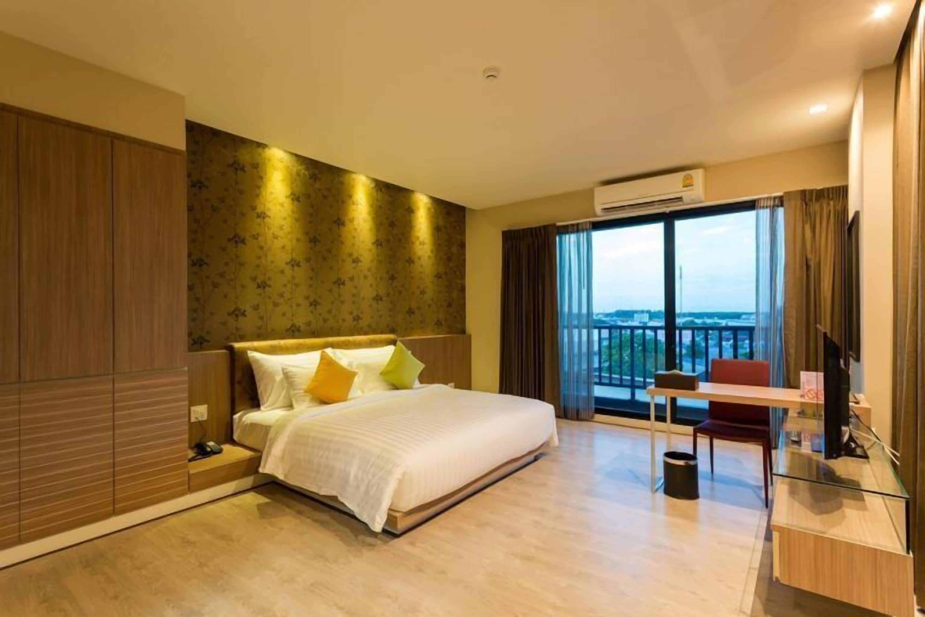 Habitación de hotel con una cama grande, un escritorio con silla, vistas a la ciudad y un equipo de aire acondicionado.
