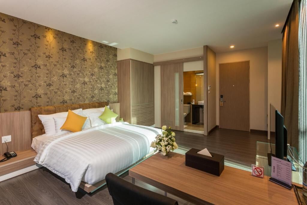 A modern hotel room with a large bed, a wooden desk, and a mirror.