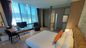 Ein Hotelzimmer mit einem großen Bett, einem Schreibtisch mit Stuhl, einem Fernseher und Blick auf die Stadt durch große Fenster.