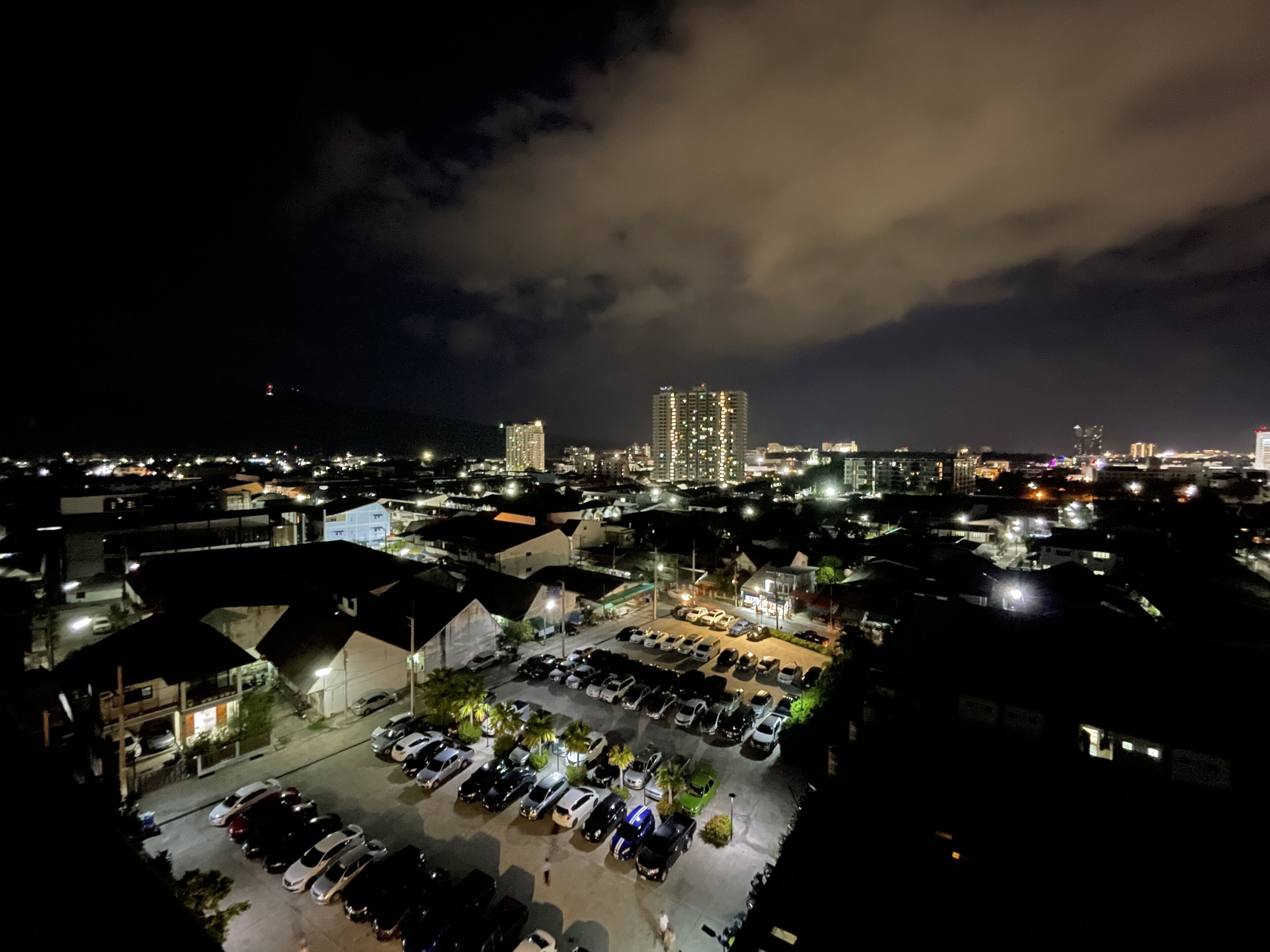 A nighttime view of a cityscape with a parking lot, buildings, and a prominent high-rise in the background.