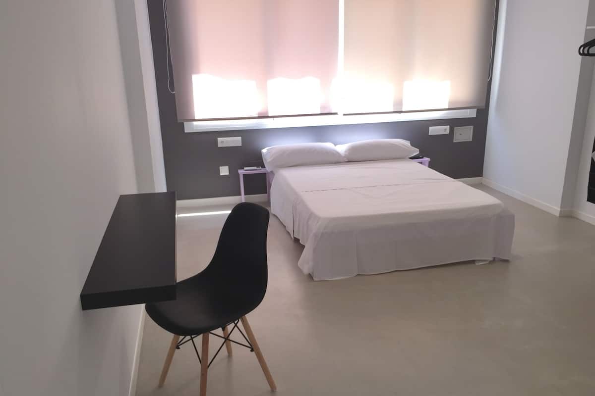 Un dormitori amb llit, escriptori i cadira.
