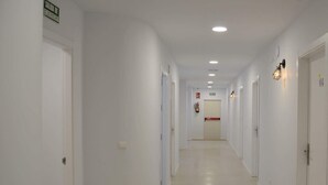 Un passadís llarg i estret amb parets blanques i portes a banda i banda, que condueix a una porta al final.