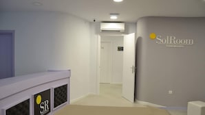 Una habitació d'hotel amb un llit blanc, una finestra petita, una porta que condueix a una altra habitació i un rètol que indica 'SolRoom' a la paret.