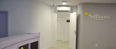 A hotel room with a white bed, a small window, a door leading to another room, and a sign indicating 'SolRoom' on the wall.