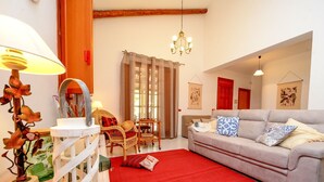 Een woonkamer met een grijze bank, een rood vloerkleed, rieten stoelen en een kroonluchter.