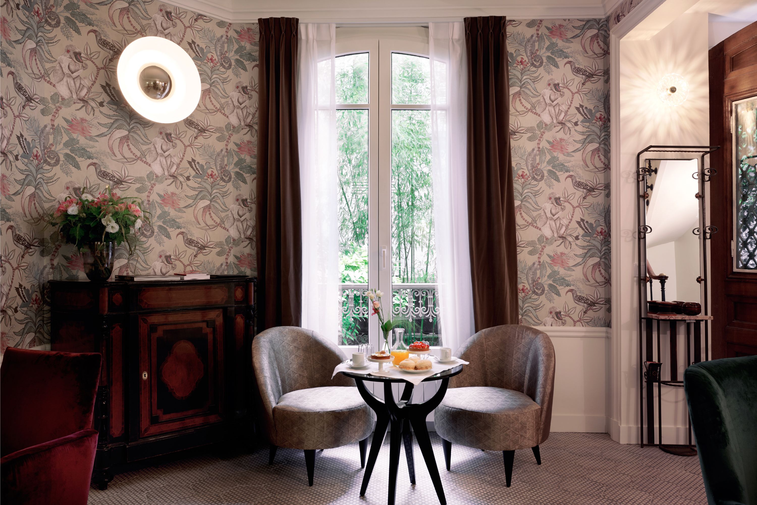 Une pièce avec une grande fenêtre, deux chaises, une table avec des éléments pour le petit-déjeuner, un miroir et un meuble.