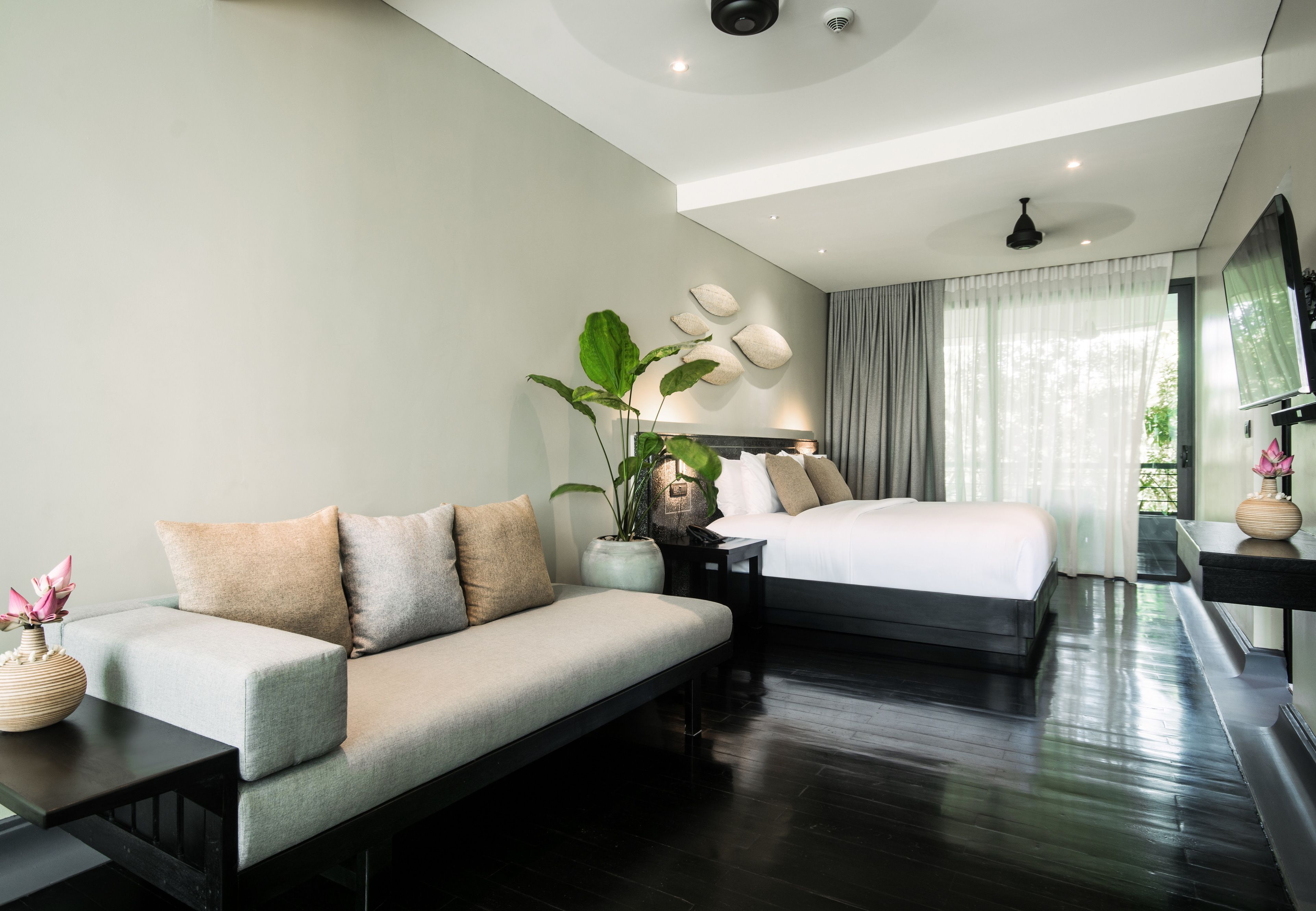 Een moderne hotelkamer met een bank, een bed, een nachtkastje, een potplant en een spiegel.