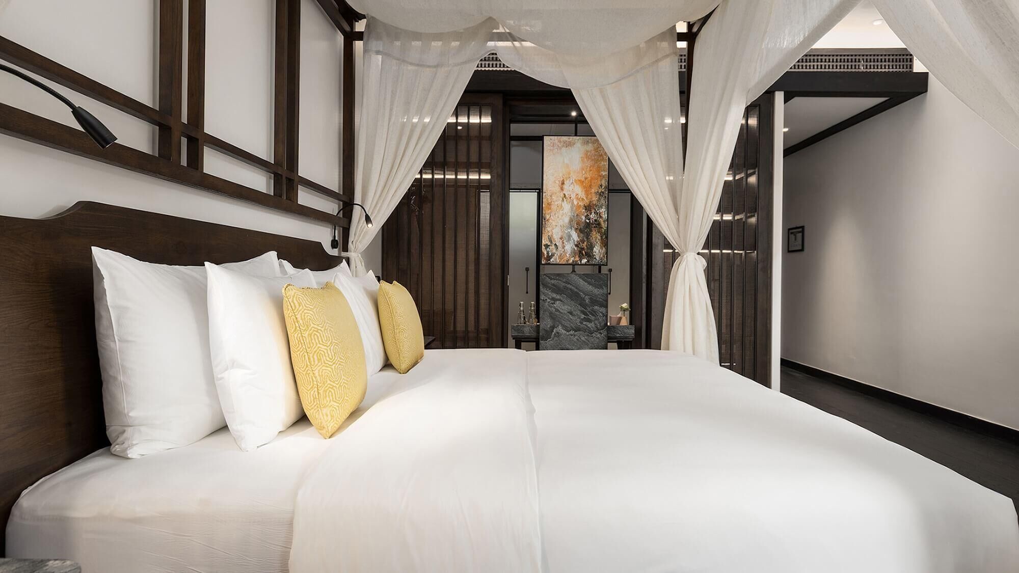 Una habitación de hotel moderna con una cama grande, ropa de cama blanca y vistas a un paisaje urbano a través de un ventanal.