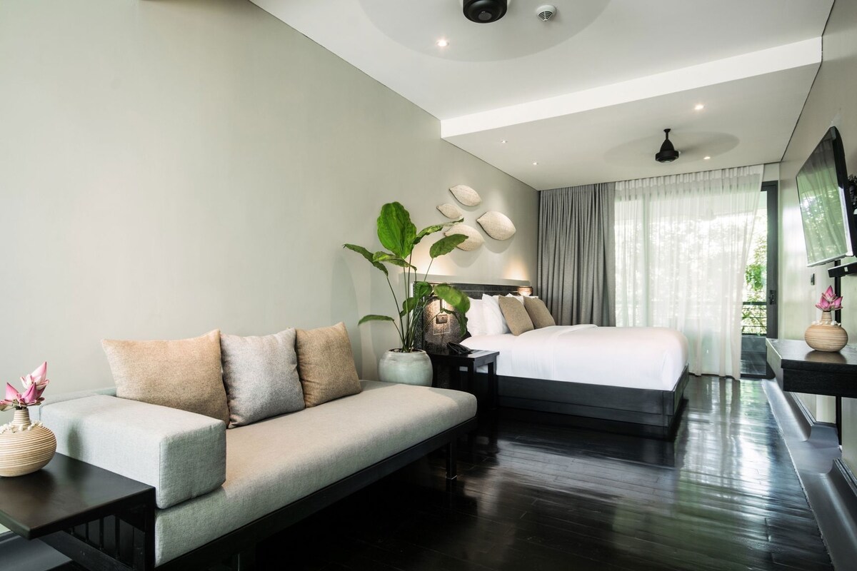 Une chambre d’hôtel moderne équipée d’un canapé, d’un lit, d’une table de chevet, d’une plante en pot et d’un téléviseur.