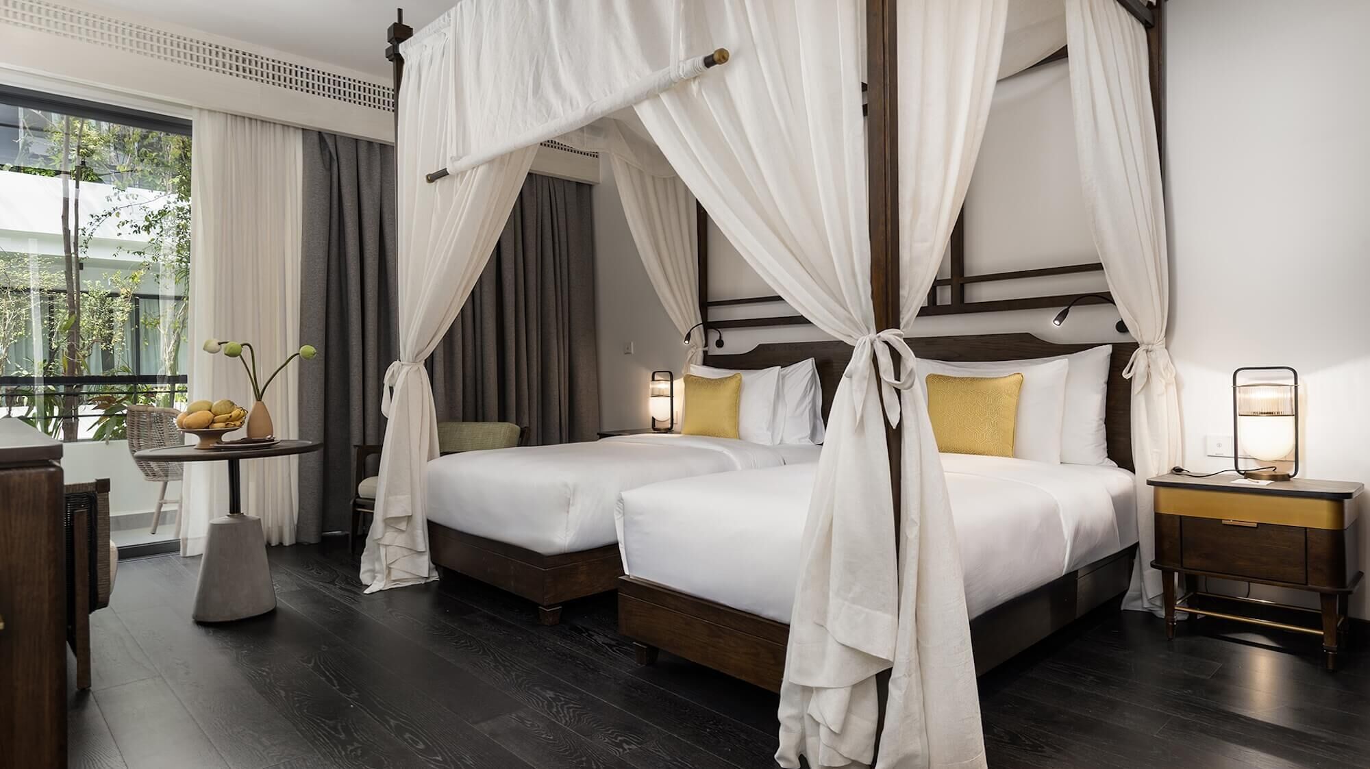 Habitaci ón de hotel con dos camas, una mesita de noche, una mesa con un jarrón de flores y vistas a zonas verdes.