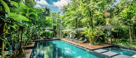Piscina rodeada por vegetação exuberante e um deck de madeira com espreguiçadeiras.