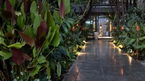 Un camino bordeado de vegetación exuberante y luces decorativas que lleva a la entrada de un edificio.