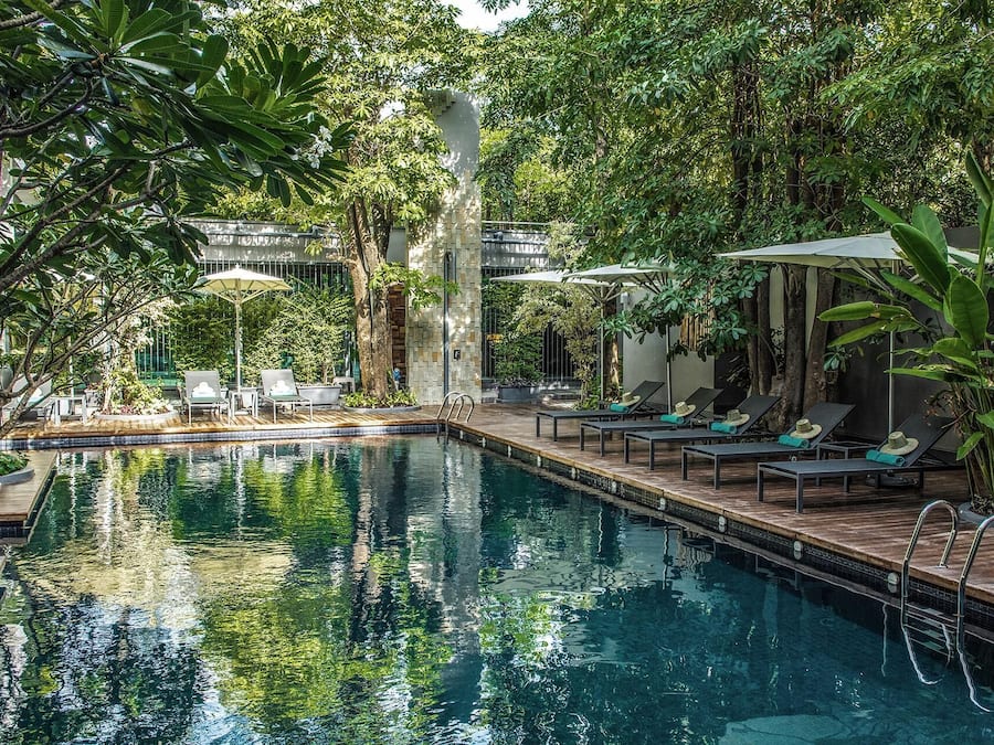 Un área de piscina interior tranquila con sillones reclinables y sombrillas, rodeada de exuberante vegetación.