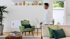 A modern living room with a sofa, armchair, and a coffee table. There are books on the table, a vase with a flower, and a potted plant. - Anjali by Syphon (Siem Reap)