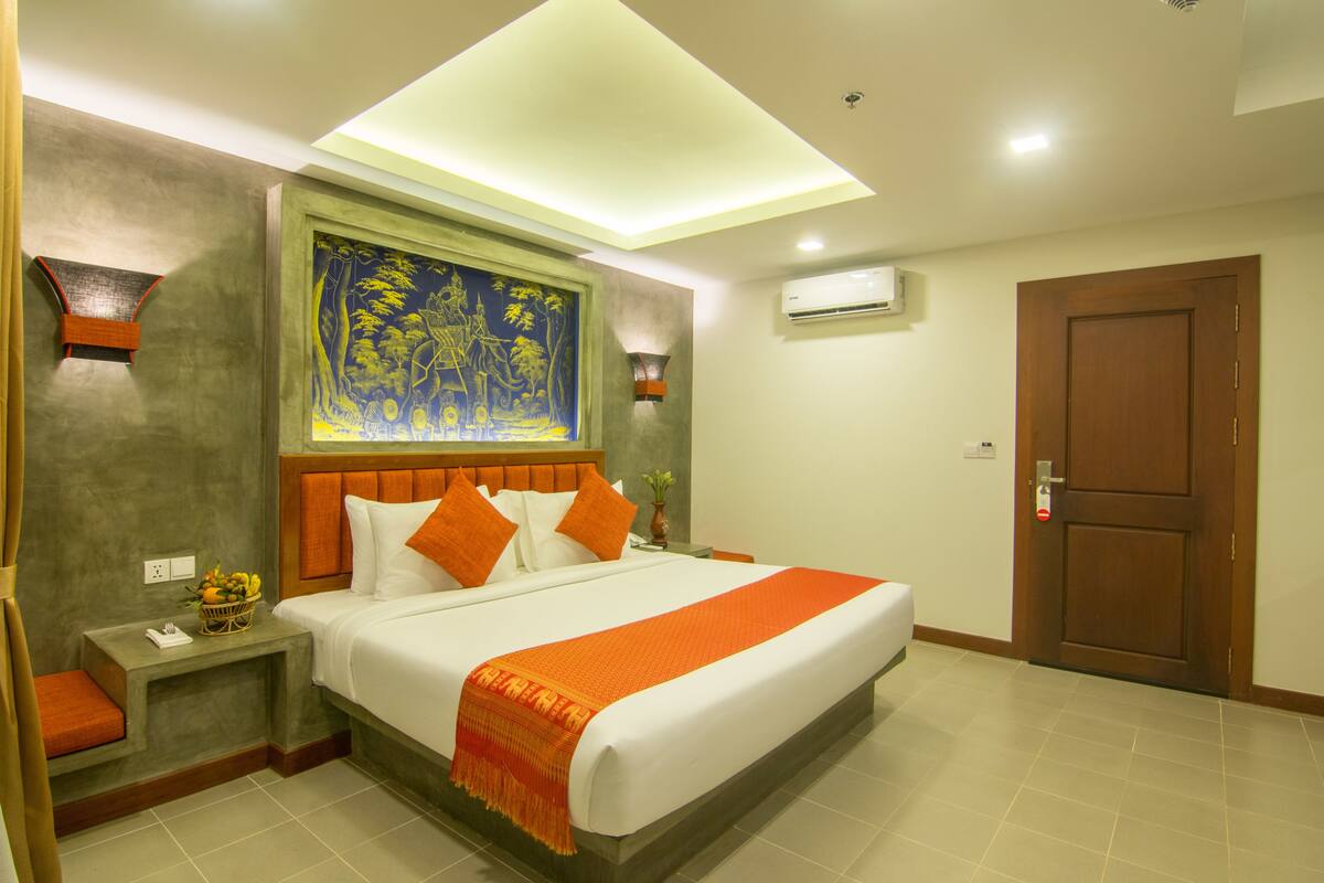 Une chambre d’hôtel avec un grand lit, un tableau au mur, un climatiseur et une porte en bois.