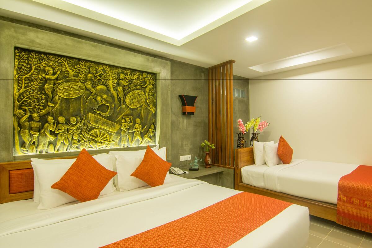 Une chambre d’hôtel avec deux lits, un grand mur décoratif, une petite table avec un vase de fleurs et un miroir.