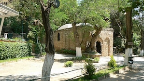 Un bâtiment en pierre doté d’une entrée en arc de cercle, entouré d’arbres et bordé d’un chemin pavé.