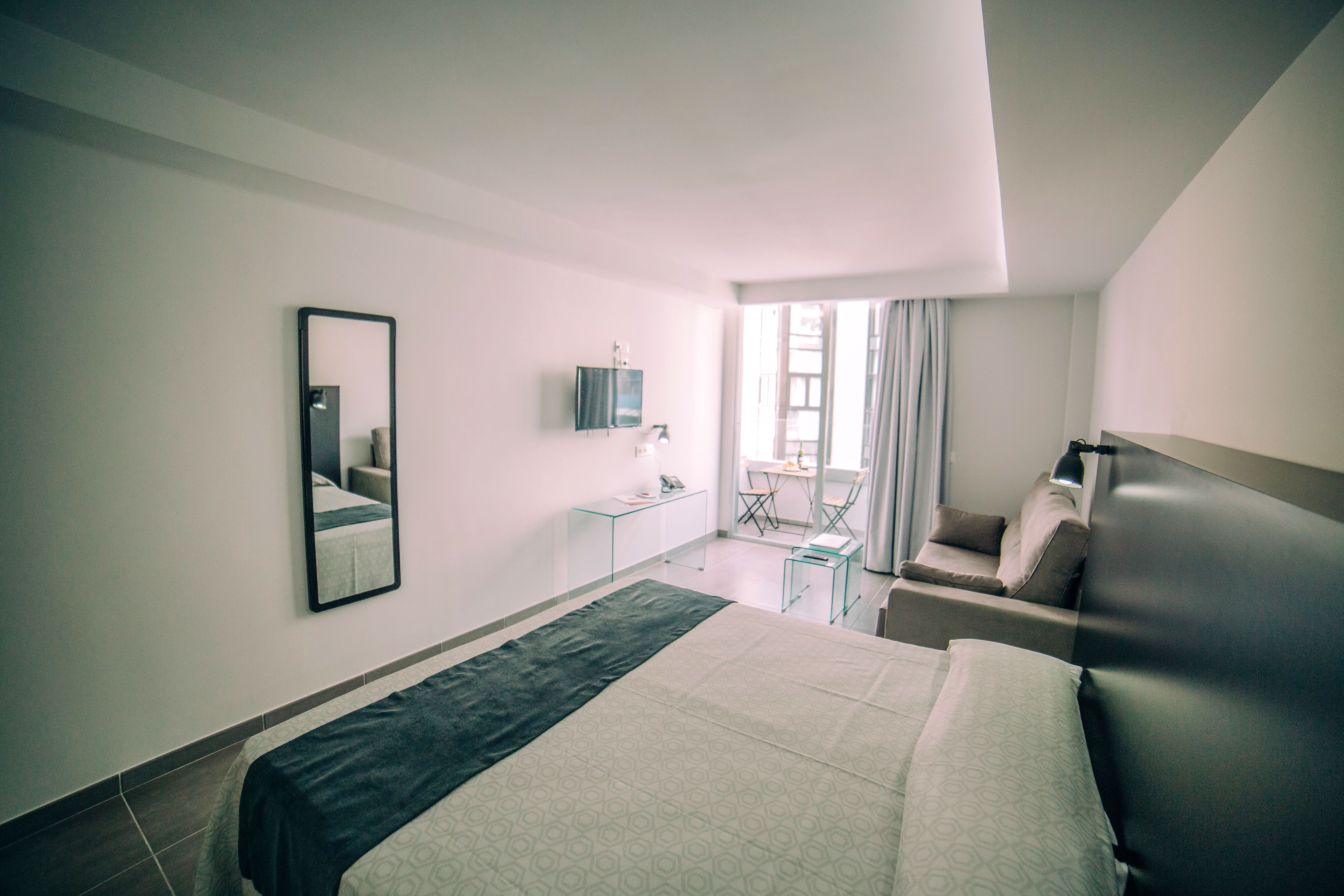 A hotel room with a bed, a desk, a chair, a mirror, and a window with curtains.
