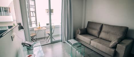 A modern living room with a grey sofa, a glass coffee table, and a desk with a laptop and phone.